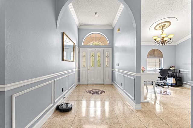 foyer entrance with a notable chandelier, ornamental molding, a decorative wall, and a textured ceiling