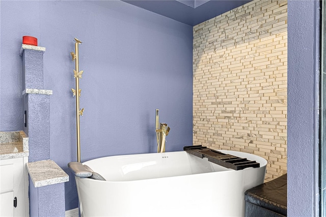 bathroom with a freestanding tub, a textured wall, and vanity