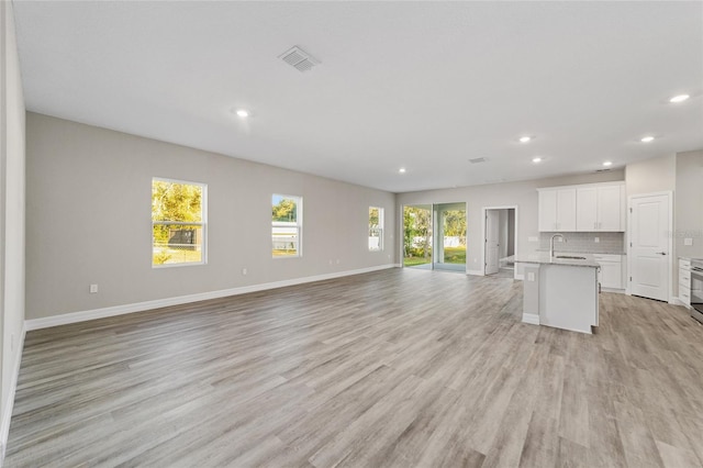 unfurnished living room featuring baseboards, visible vents, light wood-type flooring, a sink, and recessed lighting