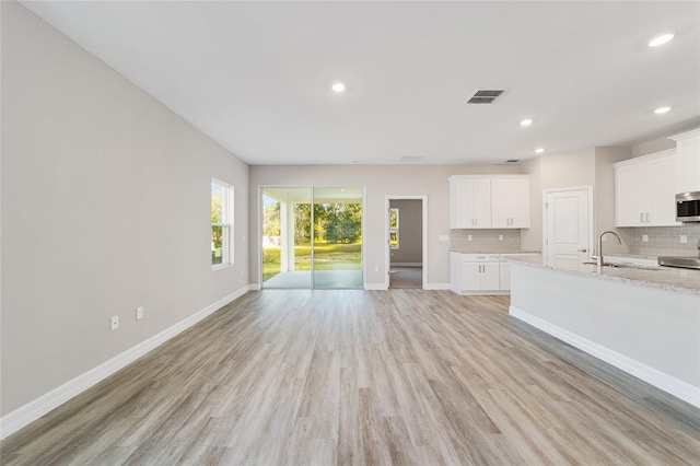 unfurnished living room featuring recessed lighting, a sink, visible vents, baseboards, and light wood finished floors