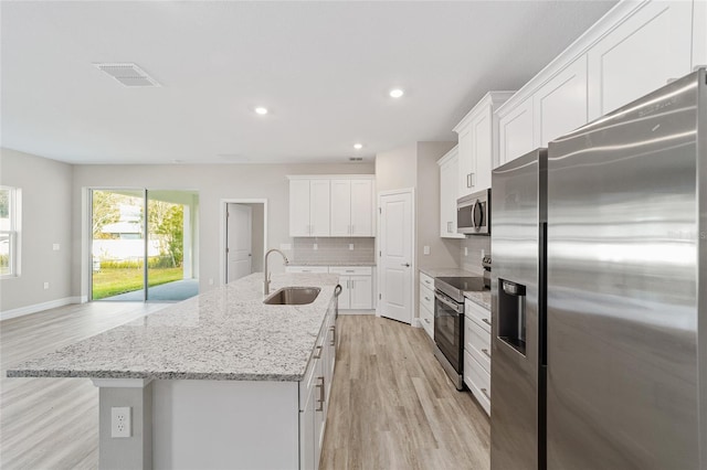 kitchen featuring a center island with sink, stainless steel appliances, light wood-style flooring, decorative backsplash, and a sink