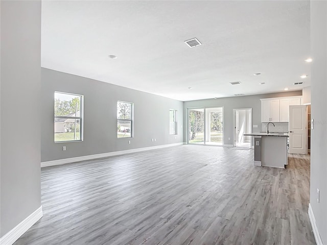 unfurnished living room with a sink, visible vents, baseboards, and a healthy amount of sunlight