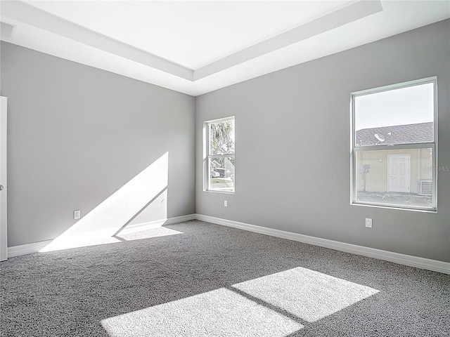 carpeted spare room featuring a raised ceiling and baseboards