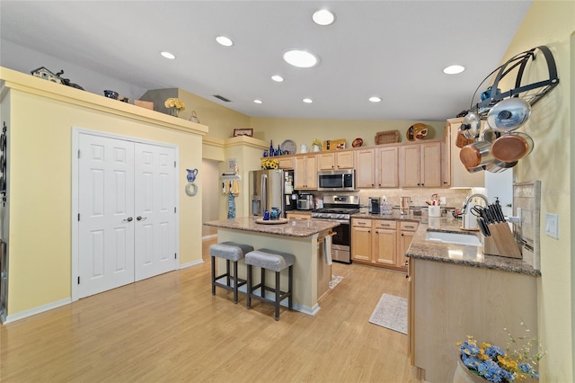 kitchen featuring lofted ceiling, stainless steel appliances, a sink, a center island, and light brown cabinetry