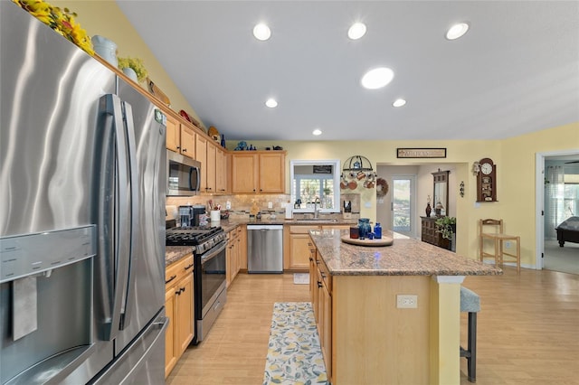 kitchen featuring light brown cabinets, appliances with stainless steel finishes, a center island, a kitchen bar, and a sink