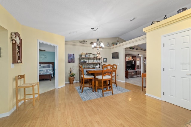 dining room featuring light wood finished floors, visible vents, vaulted ceiling, and a notable chandelier