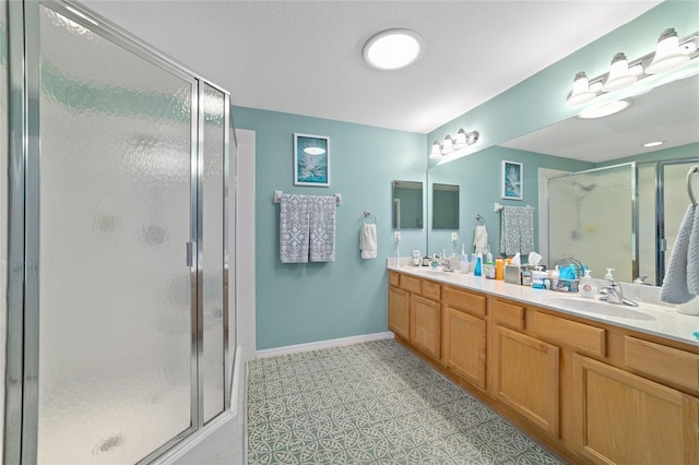 bathroom featuring double vanity, a stall shower, a sink, and baseboards