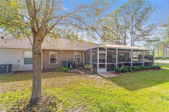 rear view of house with central air condition unit, stucco siding, a sunroom, and a yard