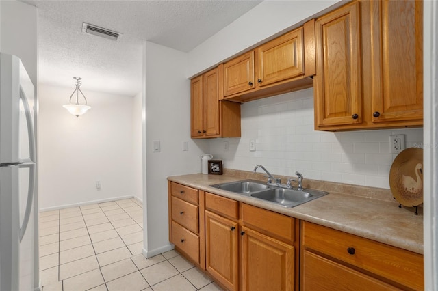 kitchen featuring light tile patterned floors, visible vents, decorative backsplash, freestanding refrigerator, and a sink