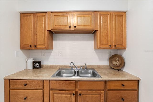 kitchen featuring light countertops, backsplash, a sink, and brown cabinets