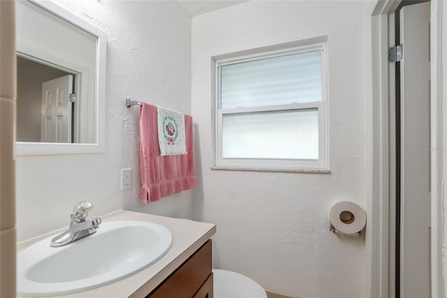 bathroom with toilet, a textured wall, and vanity