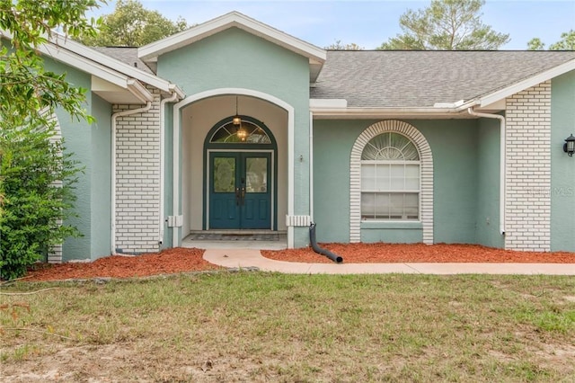 entrance to property with a yard, french doors, roof with shingles, and stucco siding