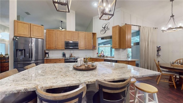 kitchen featuring lofted ceiling, a kitchen island, appliances with stainless steel finishes, light stone countertops, and backsplash