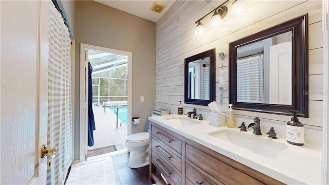 bathroom featuring a sink, wooden walls, toilet, and double vanity