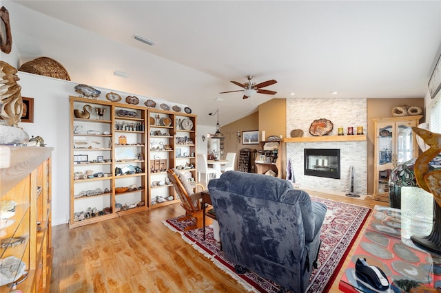 living room with a fireplace, visible vents, a ceiling fan, vaulted ceiling, and light wood finished floors