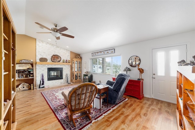 living area featuring vaulted ceiling, ceiling fan, a stone fireplace, and light wood-type flooring