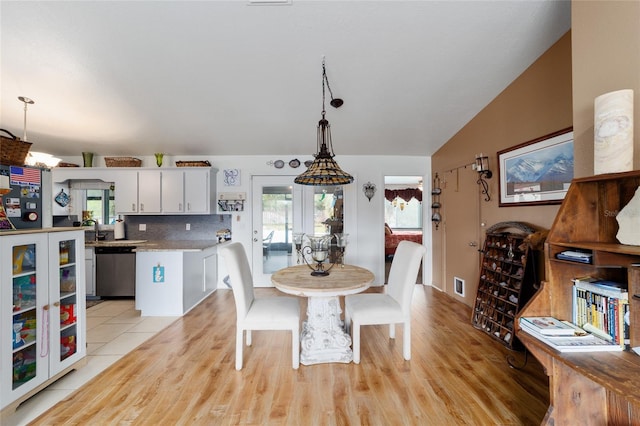 dining room featuring light wood-style floors, visible vents, and vaulted ceiling