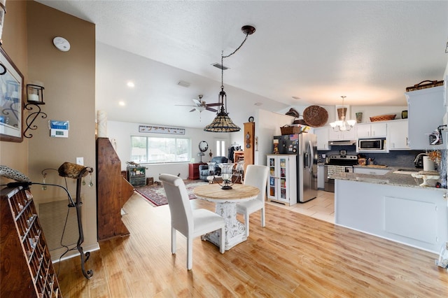 dining room with light wood-type flooring, lofted ceiling, and ceiling fan with notable chandelier