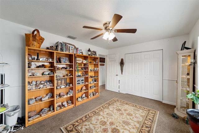 interior space with a ceiling fan, visible vents, a textured ceiling, and carpet flooring