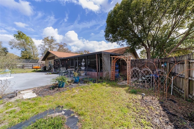 rear view of property with a yard, a patio area, a fenced backyard, and a sunroom