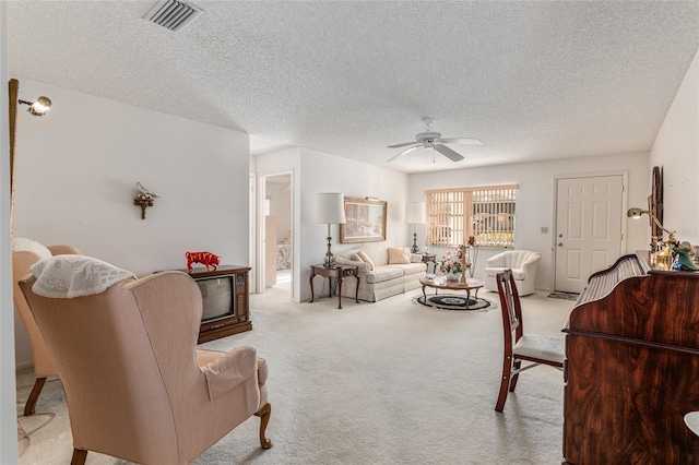 carpeted living room with ceiling fan, visible vents, and a textured ceiling