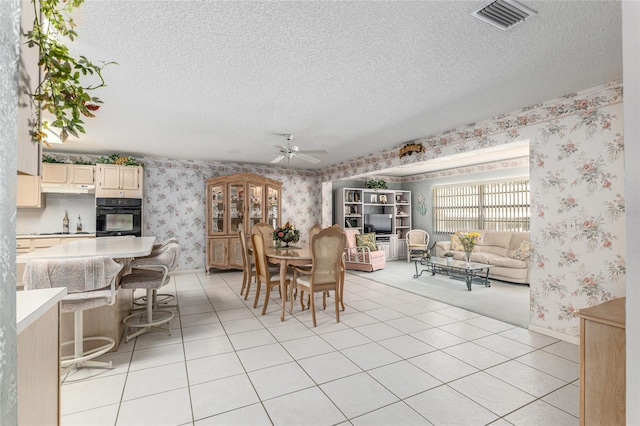 dining room with light tile patterned floors, visible vents, ceiling fan, a textured ceiling, and wallpapered walls