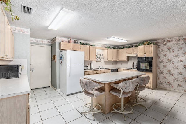 kitchen with light countertops, light brown cabinetry, a sink, black appliances, and wallpapered walls