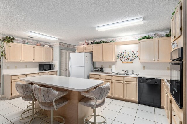 kitchen with a breakfast bar, a sink, light countertops, light brown cabinetry, and black appliances