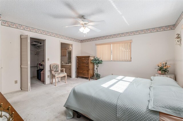 bedroom featuring a textured ceiling, connected bathroom, light colored carpet, a closet, and a walk in closet