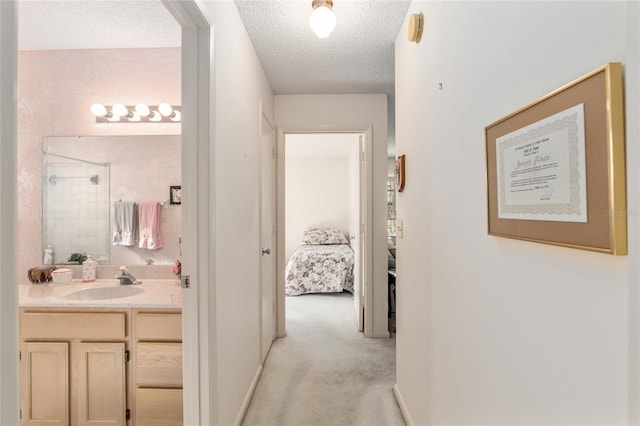 corridor with a textured ceiling, baseboards, a sink, and light colored carpet