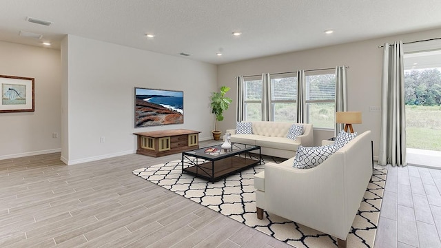 living room featuring light wood-type flooring, a healthy amount of sunlight, visible vents, and a textured ceiling