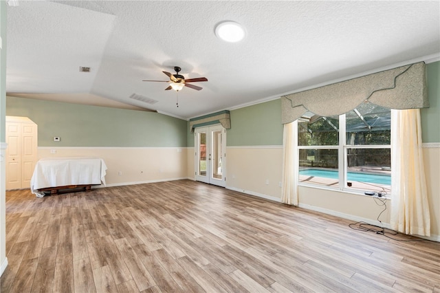 unfurnished room with light wood finished floors, visible vents, vaulted ceiling, a textured ceiling, and a ceiling fan