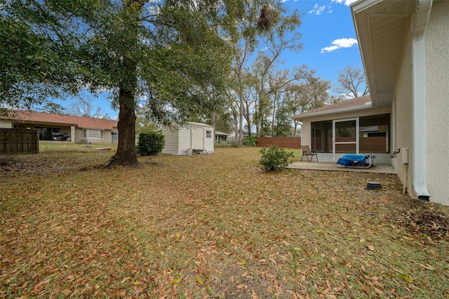 view of yard featuring a sunroom, an outbuilding, fence, a storage unit, and a patio area