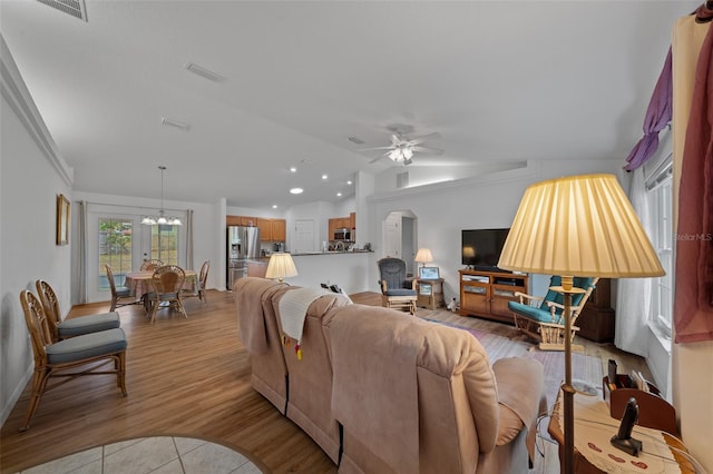 living room featuring arched walkways, light wood-style flooring, ceiling fan with notable chandelier, visible vents, and vaulted ceiling