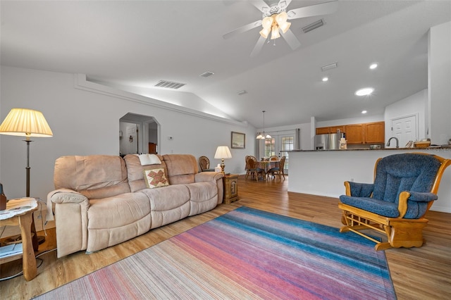 living room featuring vaulted ceiling, light wood-style flooring, and visible vents