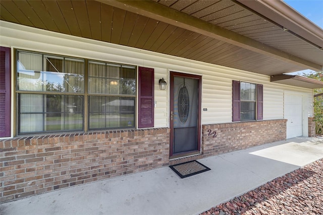 doorway to property with brick siding, covered porch, and a garage