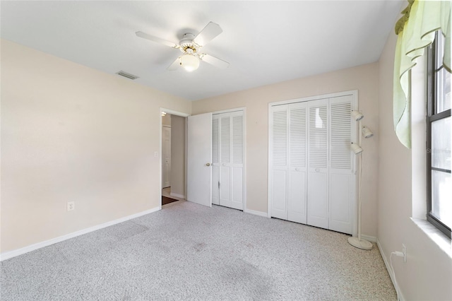 unfurnished bedroom with visible vents, two closets, carpet flooring, baseboards, and ceiling fan