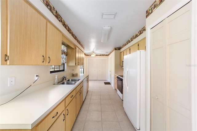 kitchen with light brown cabinetry, light countertops, light tile patterned floors, white appliances, and a sink