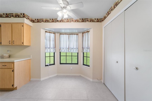 unfurnished dining area with light tile patterned flooring, a ceiling fan, and baseboards