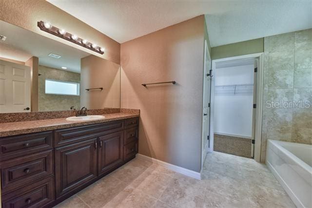 full bathroom with a bathing tub, a spacious closet, baseboards, and vanity