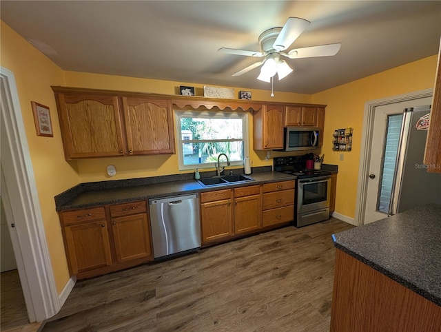 kitchen featuring dark countertops, dark wood finished floors, brown cabinetry, stainless steel appliances, and a sink