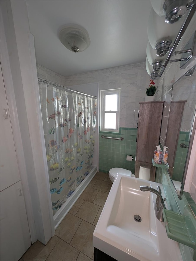 bathroom featuring toilet, a shower with curtain, tile patterned floors, tile walls, and a sink