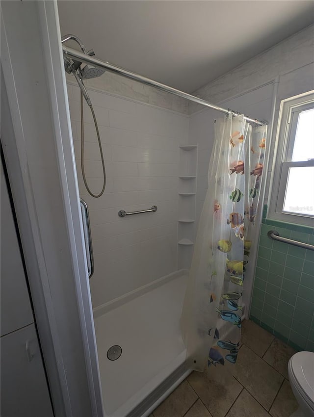 bathroom featuring tile patterned flooring, a shower stall, tile walls, and toilet