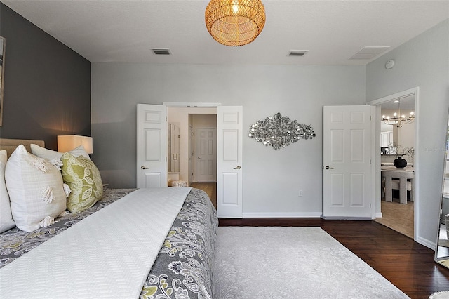 bedroom featuring an inviting chandelier, wood finished floors, visible vents, and baseboards