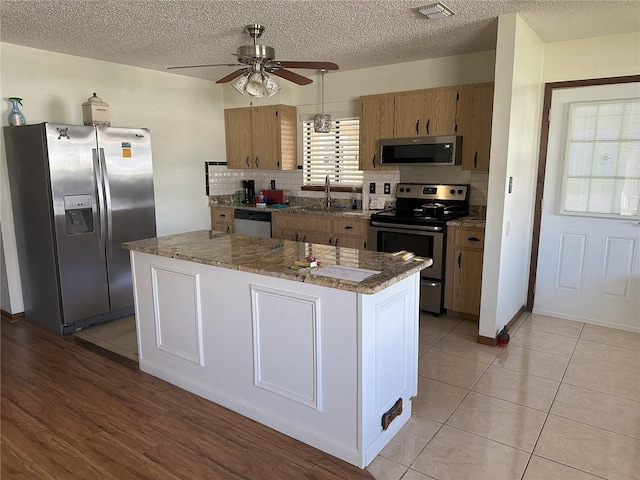 kitchen with a ceiling fan, visible vents, a sink, stainless steel appliances, and a center island