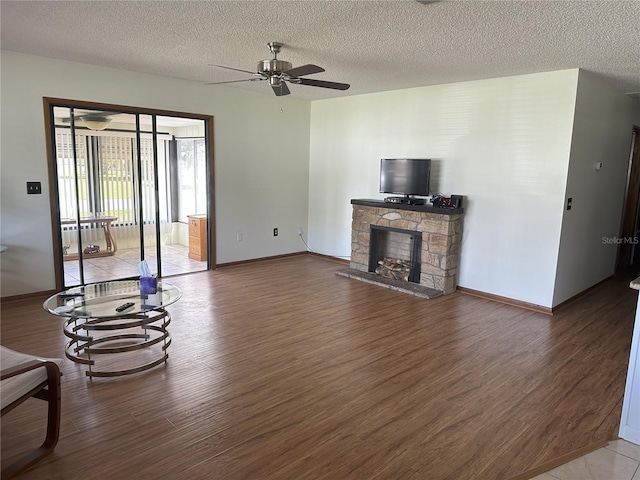 living room featuring a ceiling fan, a textured ceiling, wood finished floors, a fireplace, and baseboards