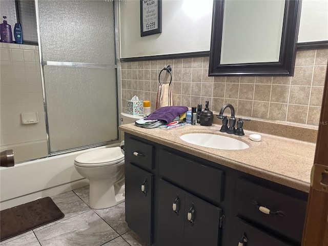 bathroom featuring bath / shower combo with glass door, toilet, tile walls, and vanity