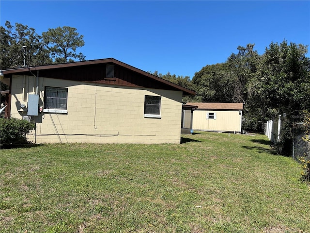 view of side of property featuring concrete block siding, a lawn, and fence