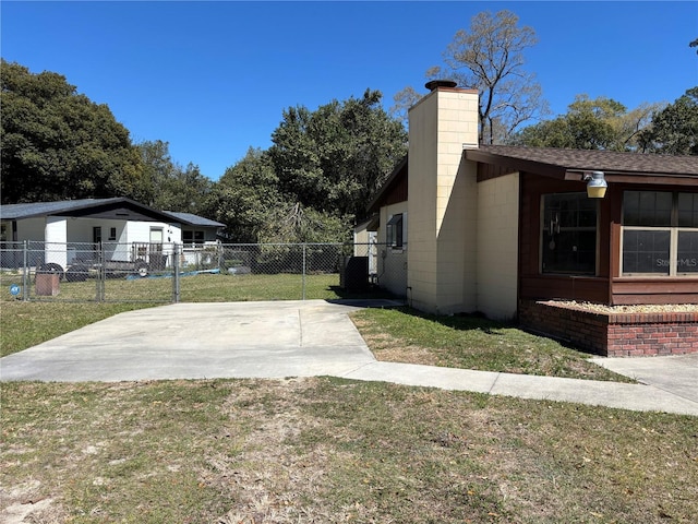 view of home's exterior featuring concrete block siding, a lawn, a chimney, and fence