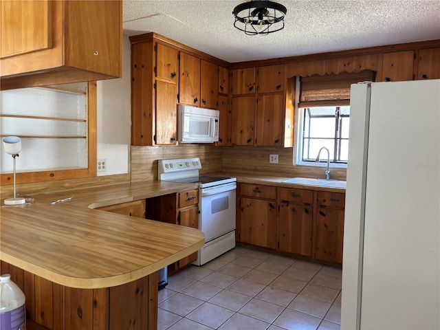 kitchen with a peninsula, white appliances, a sink, light countertops, and brown cabinets